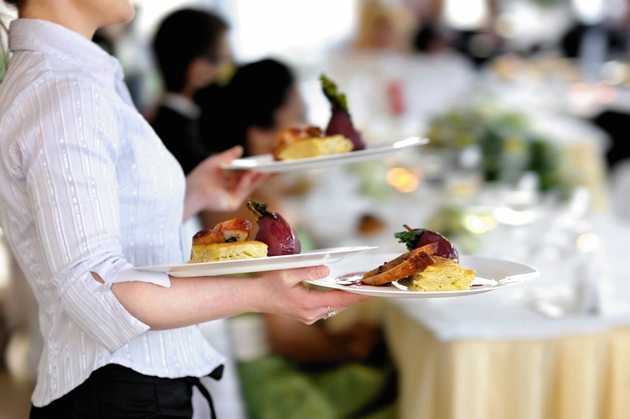 Server holding 3 dishes in there hands about to serve guests